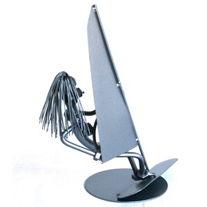 May include: A silver metal sculpture of a person windsurfing. The sculpture is made of recycled metal and is a unique and whimsical piece of art.