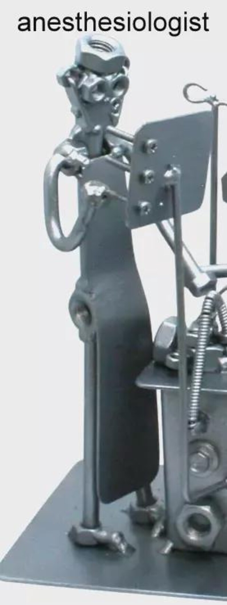 May include: A metal sculpture of an anesthesiologist constructed from various hardware components including nuts, bolts, and metal plates. The figure stands on a flat base, holding a rectangular plate, with the word anesthesiologist printed above.