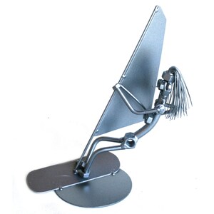 May include: A silver metal sculpture of a person windsurfing. The sculpture is made of nuts, bolts, and wire. The person is holding a sail and is standing on a board.