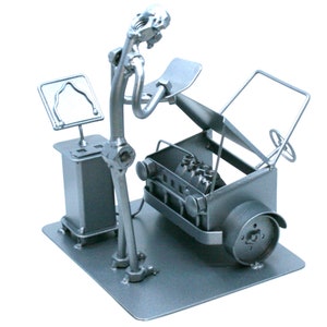 May include: A silver metal sculpture of a mechanic working on a car. The mechanic is made of nuts, bolts, and other metal pieces. The car is also made of metal and has an open hood.