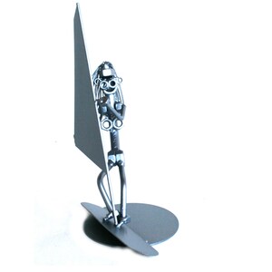May include: A silver metal sculpture of a person windsurfing. The sculpture is made of nuts, bolts, and other metal pieces. The person is holding a sail and standing on a surfboard.
