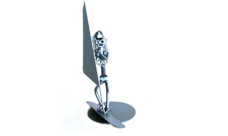 May include: A silver metal sculpture of a person windsurfing. The sculpture is made of nuts, bolts, and other metal pieces. The person is holding a sail and standing on a surfboard.