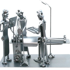 Peut inclure: Une sculpture en métal argenté représentant une scène médicale avec trois personnages fabriqués à partir d'écrous, de boulons et de pièces métalliques. Les personnages sont disposés autour d'une table d'opération avec une potence.