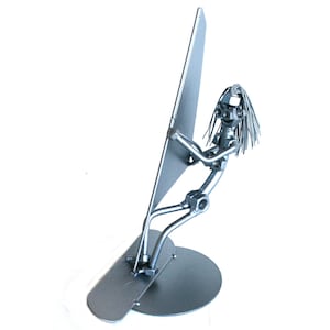 May include: A silver metal sculpture of a person windsurfing. The sculpture is made of nuts, bolts, and other metal pieces. The person is holding a sail and is standing on a board.