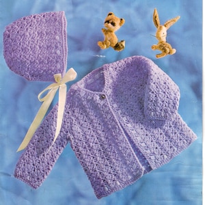 May include: A purple crocheted baby cardigan with a matching bonnet and white ribbon. The cardigan has a button closure and a textured stitch pattern.
