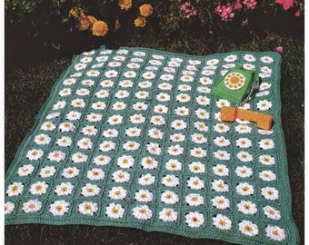 May include: A green crocheted blanket with a daisy pattern. The blanket is laid out on a grassy surface with a green toy telephone and a yellow toy phone receiver on top of it.