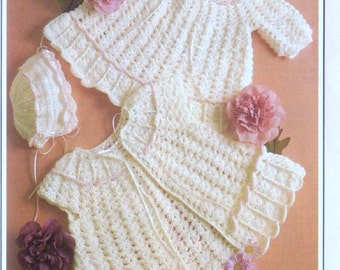 May include: Two crocheted baby outfits in white with pink trim. One outfit is a jacket with long sleeves and the other is a dress with short sleeves. A white crocheted hat with pink trim is also included.