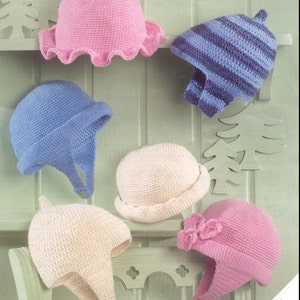 Può includere: Sei cappelli all'uncinetto in vari colori e stili, tra cui rosa, blu e crema. Alcuni cappelli hanno le alette per le orecchie, mentre altri hanno un bordo. I cappelli sono esposti su uno scaffale bianco e una sedia bianca.
