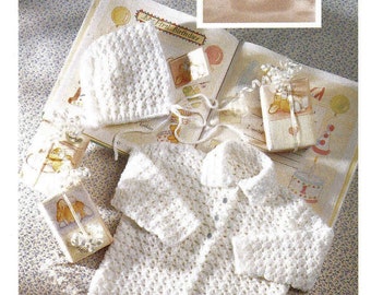 May include: A white crocheted baby cardigan with a button closure, a matching white crocheted hat, and a book with the text "My First Birthday".