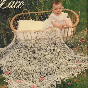 Könnte beinhalten: Ein weißer Häkel-Spitzen-Schal mit einem zarten Blumenmuster. Der Schal liegt über einem Weidenkorb mit einem Baby, das ein weißes Kleid trägt.