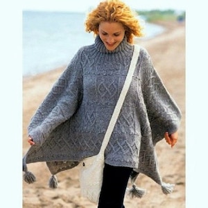 May include: A gray knitted poncho with a turtleneck and a white strap. The poncho has a geometric pattern and tassels on the edges.