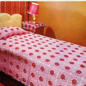 Peut inclure: Une couvre-lit en crochet rose avec un motif floral. La couvre-lit est sur un lit avec une tête de lit blanche et un oreiller rose.