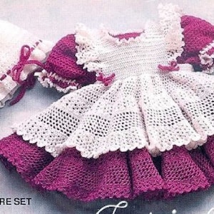 May include: A white crocheted baby dress with a pink crocheted bodice and a white crocheted hat. The dress has a ruffled hem and the hat has a pink ribbon.