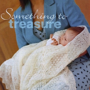 Może przedstawiać: Kobieta w niebieskim żakiecie trzyma dziecko owinięte w biały, szydełkowy szal chrzcielny, znany również jako szal pajęczynowy. Tekst "Something to treasure" jest napisany ozdobnym fontem nad dzieckiem.