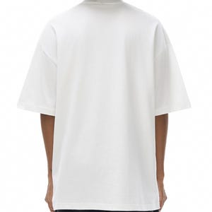 K&ouml;nnte beinhalten: Ein schlichtes, wei&szlig;es T-Shirt mit kurzen &Auml;rmeln und Rundhalsausschnitt. Das Kleidungsst&uuml;ck hat eine lockere, entspannte Passform mit &uuml;berschnittenen Schultern und einem geraden Saum. Der Stoff ist einfarbig wei&szlig; und ohne Muster oder Logos.