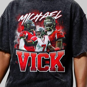 May include: A black t-shirt with a faded, vintage look featuring a graphic of Michael Vick in a red and black Atlanta Falcons jersey. The text "MICHAEL VICK" is printed in red and white.