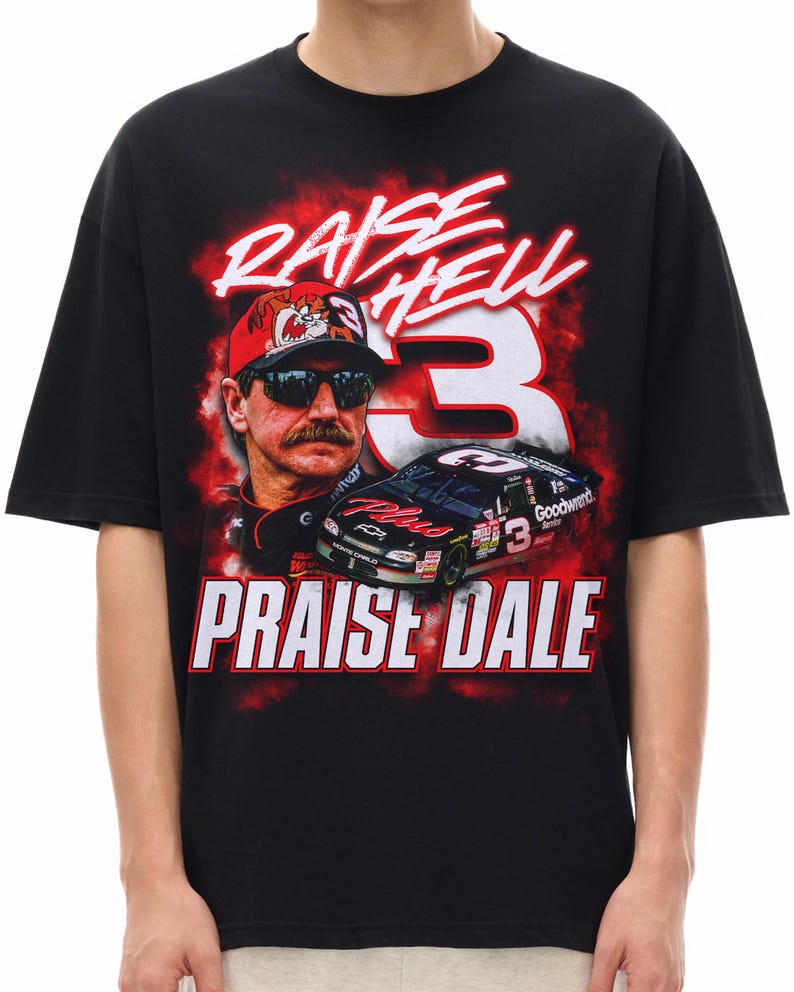 K&ouml;nnte beinhalten: Ein schwarzes Kurzarm-T-Shirt mit einem Grafikdruck eines Rennfahrers mit Sonnenbrille und roter Kappe, einem schwarzen Rennwagen mit der Nummer 3 und roten Raucheffekten. Der Text lautet RAISE HELL und PRAISE DALE in wei&szlig;er und roter Schrift.