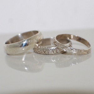 May include: Three silver rings, one plain and two with intricate floral designs.