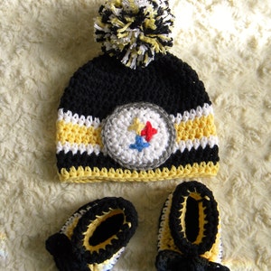 May include: Black, yellow, and white crocheted baby hat with a pom-pom and matching booties. The hat features a Pittsburgh Steelers logo.