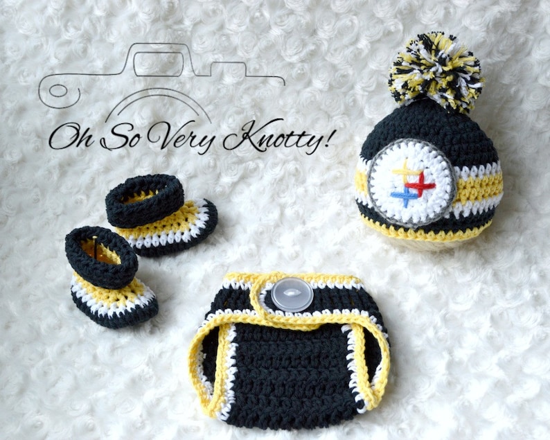 May include: A crocheted baby outfit in black, yellow, and white with a Pittsburgh Penguins logo on the hat. The outfit includes a hat, diaper cover, and booties.