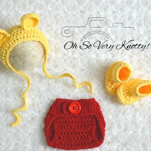 May include: A crocheted baby outfit in yellow and red. The outfit includes a bear hat, diaper cover, and booties. The hat has long ties that can be tied under the chin. The diaper cover has a red button. The booties are yellow with orange accents.
