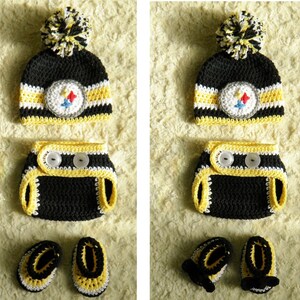 May include: A black, yellow, and white crocheted baby outfit set with a hat, diaper cover, and booties. The hat has a black pom-pom on top and a Steelers logo on the front.
