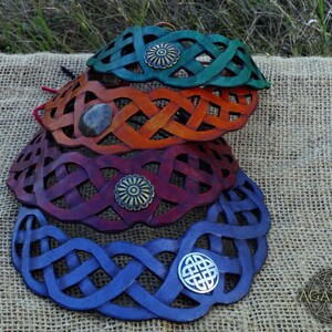 May include: Four leather Celtic knot headbands in different colors: green, orange, burgundy, and blue. Each headband has a metal accent in the center.