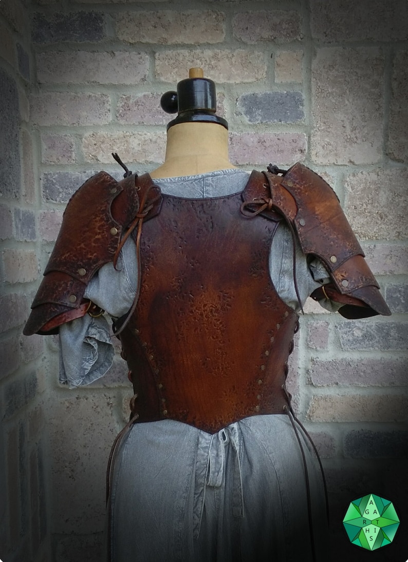 May include: Brown leather armor with a textured finish. The armor includes a chest piece and shoulder pads. The armor is displayed on a mannequin against a brick wall.