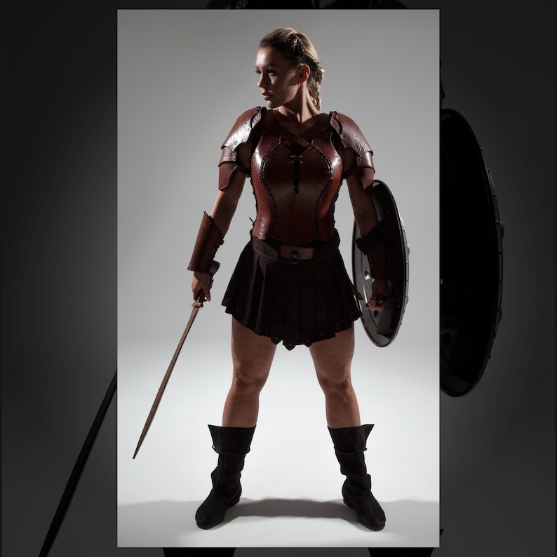 May include: A woman wearing brown leather armor, a black skirt, and brown boots holds a sword and a shield. She is standing in a studio setting with a white background.