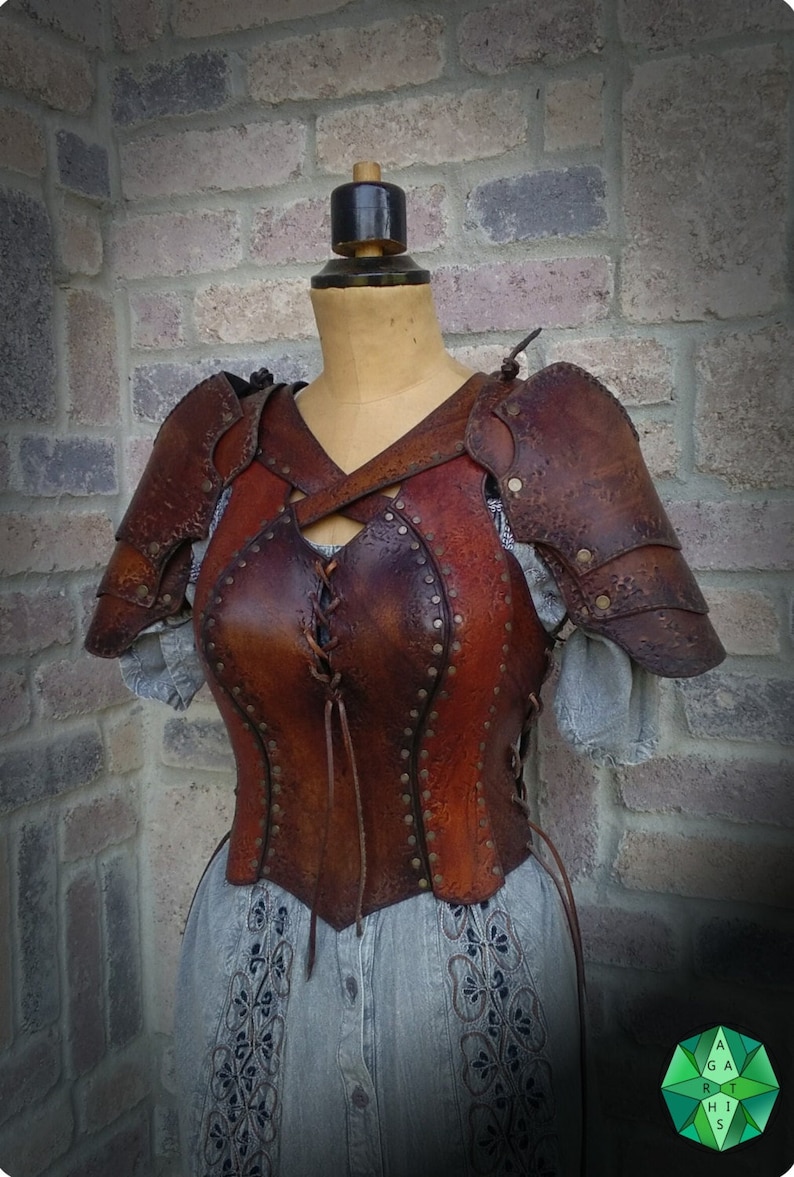 May include: Brown leather armor with a laced front and studded details. The armor is worn on a mannequin with a gray dress.