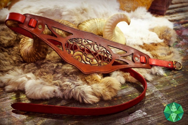 May include: A brown leather collar with intricate cutouts and a red leather strap. The collar is lying on a white and brown fur surface.