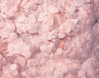 Puede incluir: Una densa colección de pequeños confetis de papel de color rosa claro con forma circular. Los discos individuales están superpuestos, creando una superficie texturizada con variados tonos de rosa suave y sombras sutiles en la composición.