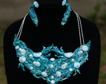 May include: A turquoise and white necklace and earrings set with a swirling, organic design. The necklace features a large, statement piece with white pearl-like accents. The earrings are smaller versions of the necklace design.