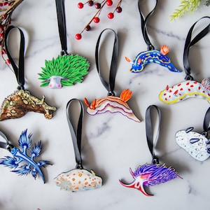 Puede incluir: Una colecci&oacute;n de adornos de babosas marinas coloridas con cintas negras. Los adornos presentan varios dise&ntilde;os, incluyendo patrones azules, naranjas y blancos. Los adornos miden aproximadamente 7.6 cm de largo.