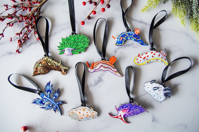 Puede incluir: Una colecci&oacute;n de adornos de babosas marinas coloridas con cintas negras. Los adornos presentan varios dise&ntilde;os, incluyendo patrones azules, naranjas y blancos. Los adornos miden aproximadamente 7.6 cm de largo.