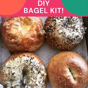 May include: Four homemade bagels, two with sesame seeds and poppy seeds, one with cheese and one plain. The bagels are on a white surface with the text "DIY BAGEL KIT!" above them.