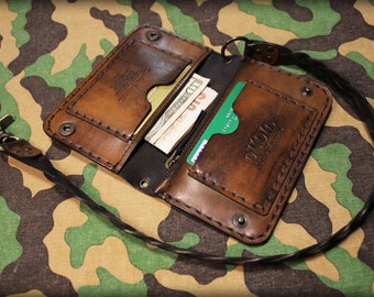 May include: A brown leather wallet with a braided strap and a zippered pocket. The wallet is open and shows a credit card and cash inside. The wallet has the word "STUDIO" embossed on the front.