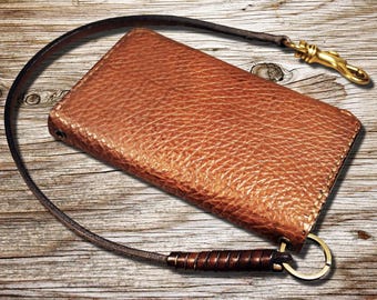 May include: A brown leather wallet with a strap and a brass hook. The wallet has a textured surface and is attached to a brown leather strap with a brass hook.