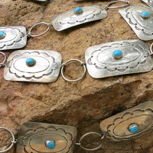 May include: A silver belt with turquoise stones set in rectangular silver plaques. The belt is made of linked silver rings.