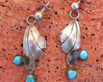 May include: A pair of silver earrings with a leaf design and turquoise stones. The earrings have a post back and a small silver ball above the leaf. The turquoise stones are round and set in silver.