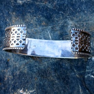 May include: A silver bracelet with a geometric pattern on the ends. The bracelet is open and has a smooth, polished surface.