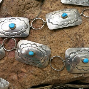 May include: A silver belt with turquoise stones set in rectangular silver plaques. The belt is made of linked silver rings.