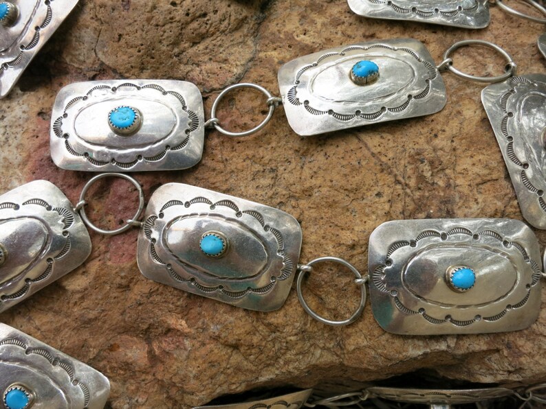 May include: A silver belt with turquoise stones set in rectangular silver plaques. The belt is made of linked silver rings.