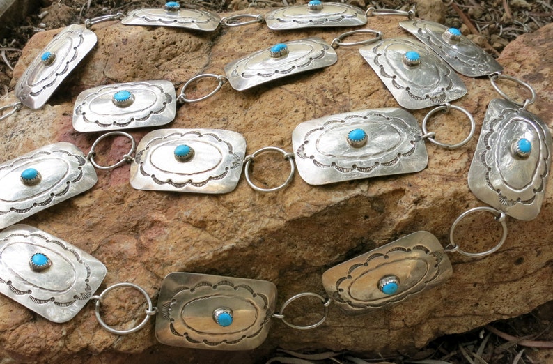 May include: A silver belt with turquoise stones set in rectangular silver plaques. The belt is made of linked silver rings.
