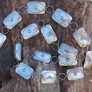 May include: A silver belt with turquoise stones set in rectangular shapes. The belt is made of linked silver pieces with a decorative design.