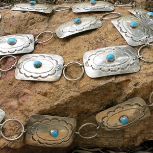 May include: A silver belt with turquoise stones set in rectangular silver plaques. The belt is made of linked silver rings.