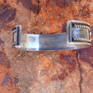 May include: Silver bracelet with a textured design and a clasp. The bracelet is marked "sterling" on the back.