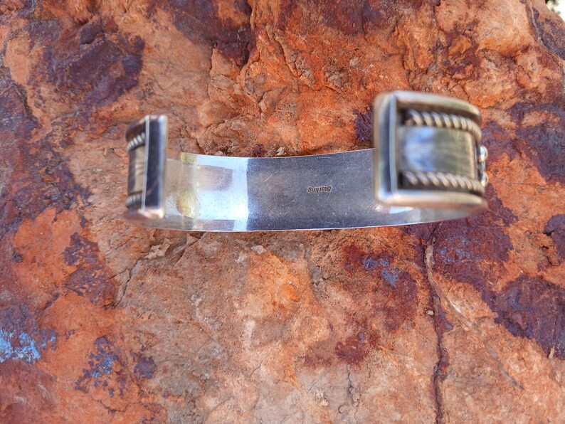 May include: Silver bracelet with a textured design and a clasp. The bracelet is marked "sterling" on the back.