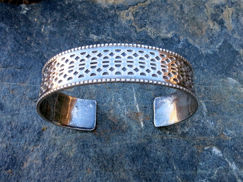 May include: A silver bracelet with a geometric pattern and a beaded edge.