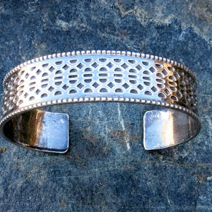May include: A silver bracelet with a geometric pattern and a beaded edge.